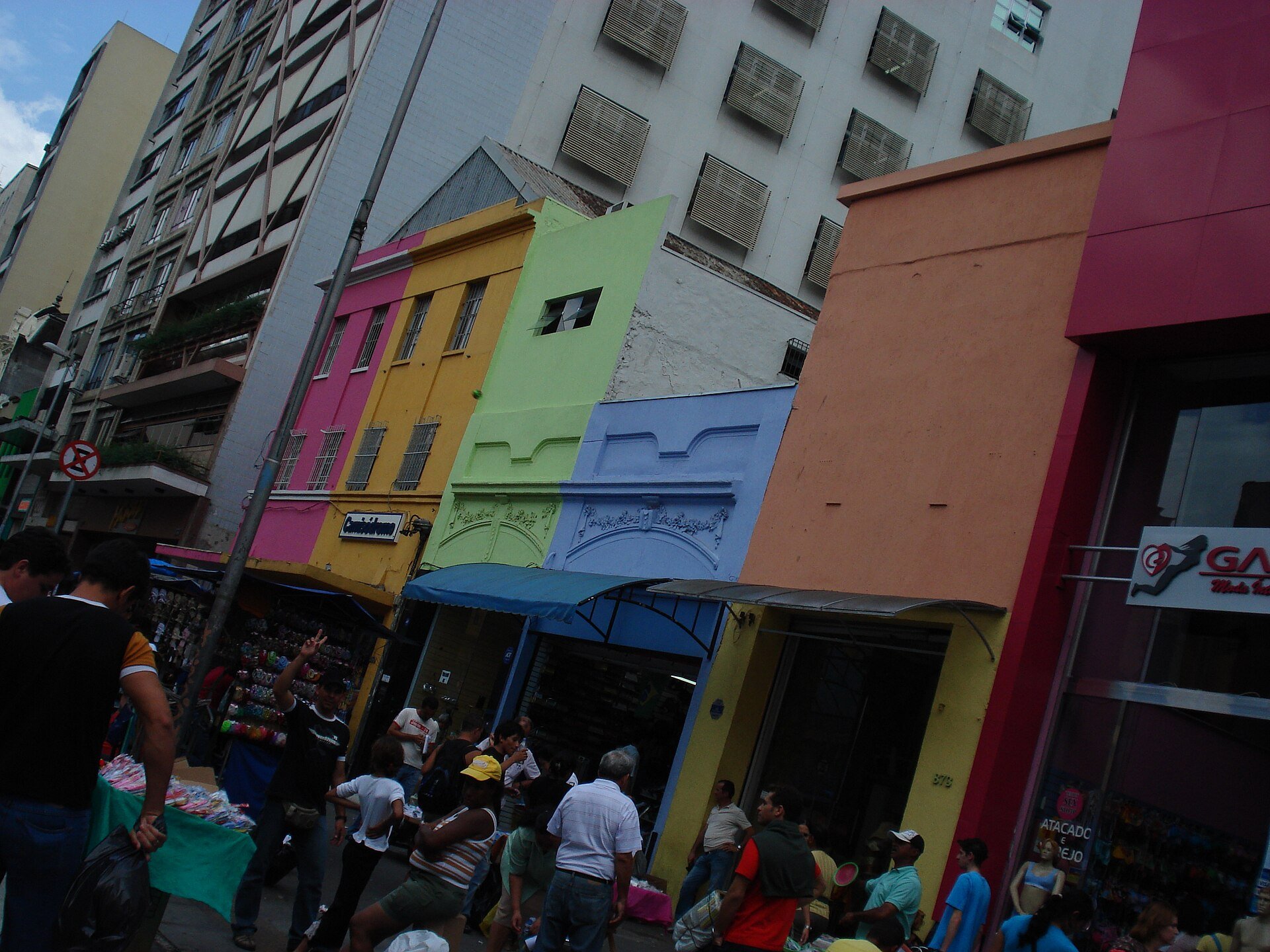 Fachadas coloridas de lojas e movimento de pedestres na Rua 25 de Março, no Centro de São Paulo