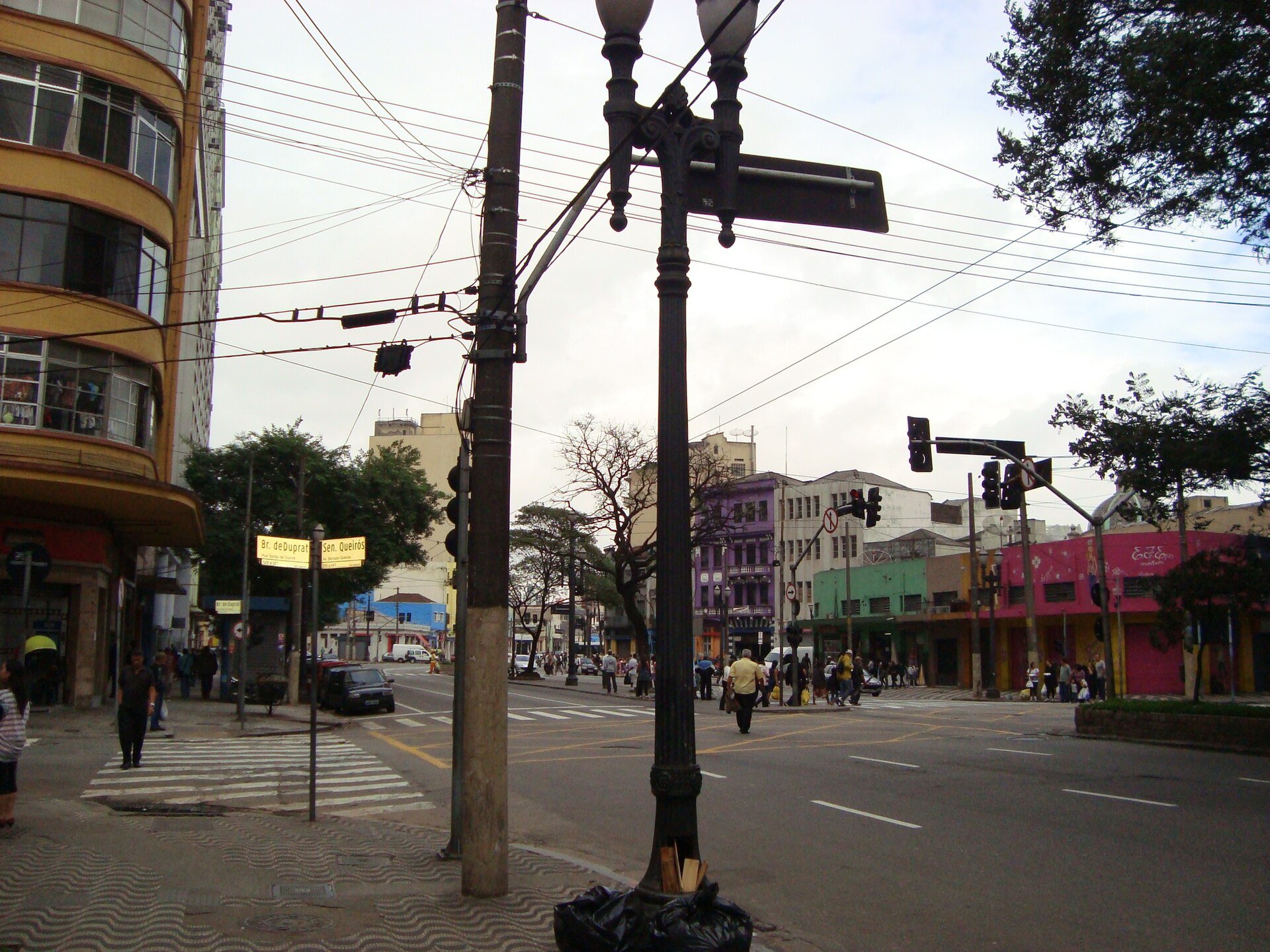 Esquina da Avenida Senador Queirós com a Rua Barão de Duprat, com lojas e pedestres, no Centro de São Paulo