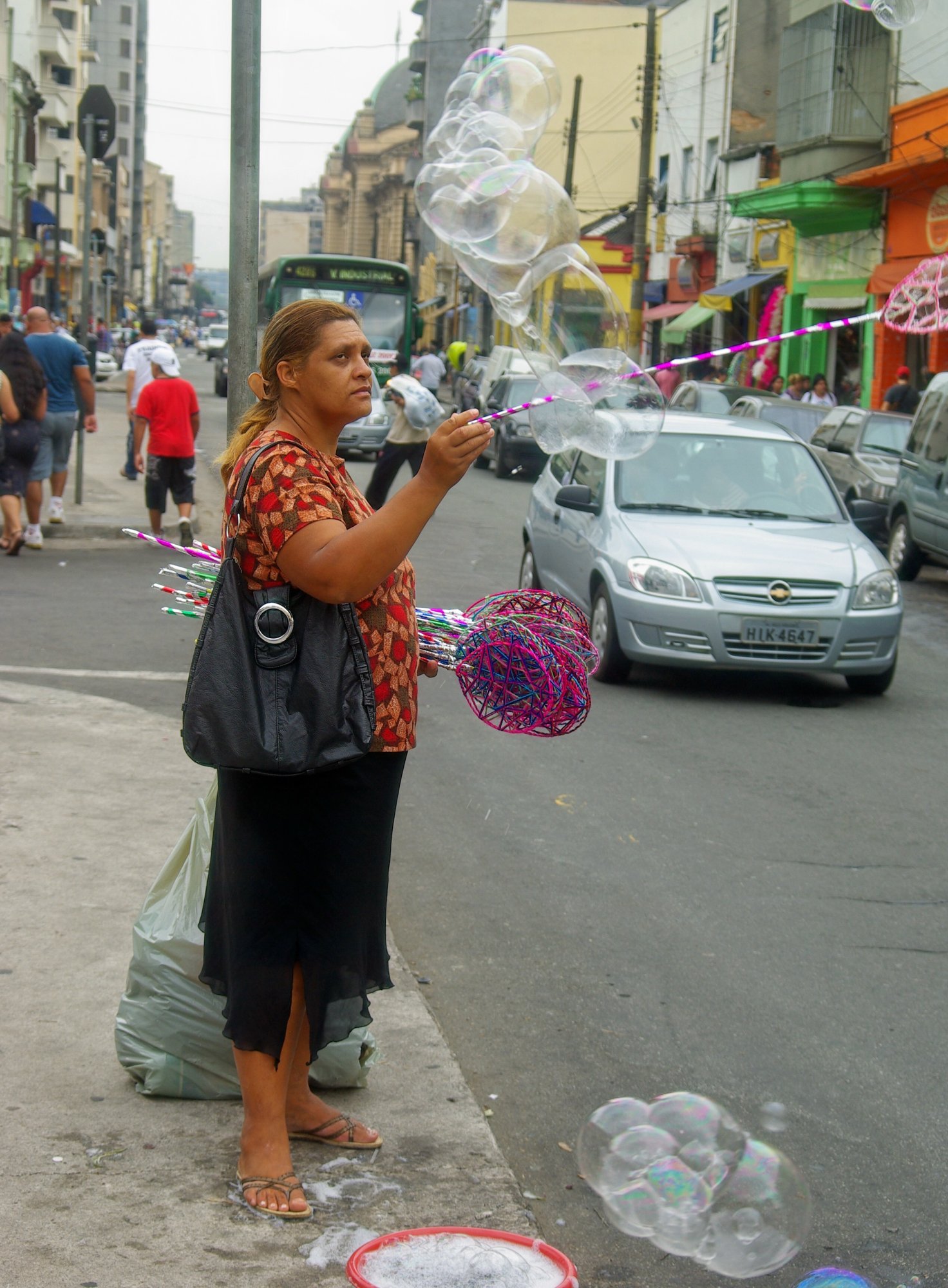 Vendedora faz bolhas de sabão gigantes com varinhas coloridas na calçada da Rua 25 de Março