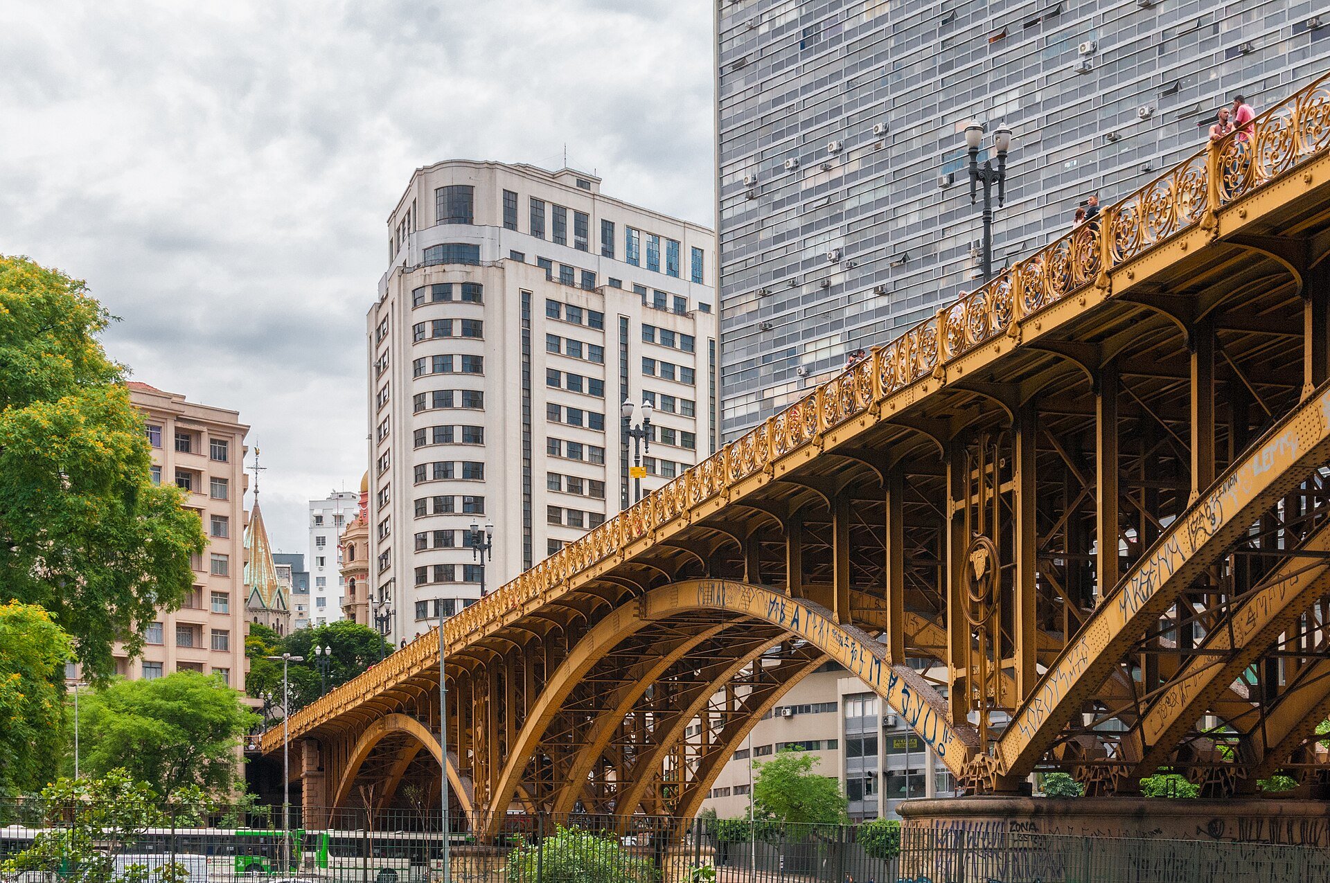 Arcos de ferro dourados do Viaduto Santa Ifigênia sobre o Vale do Anhangabaú, com prédios do centro ao fundo